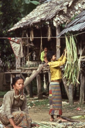 Trabajando el ratán delante de la casa comunal. La mujer que está en el primer plano está fumando un pitillo de tabaco negro enrollado en una hoja. Casi todo el mundo fumaba y el tabaco funcionaba como moneda para el intercambio.
